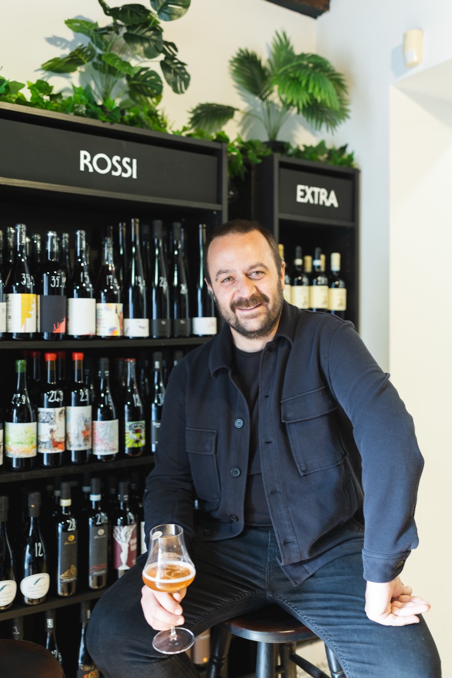 Alberto in negozio, davanti agli scaffali dei vini, con un calice in mano