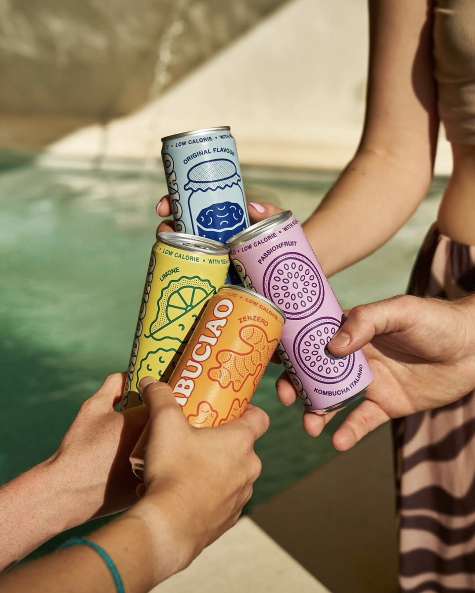 Quattro lattine di Kombuciao tenute in mano a bordo piscina