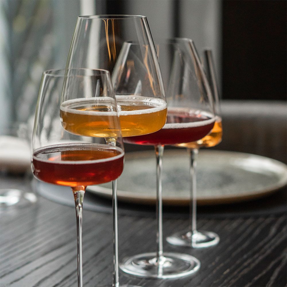 Tre calici di sparkling tea Acala, ambra e rosa, su un tavolo apparecchiato