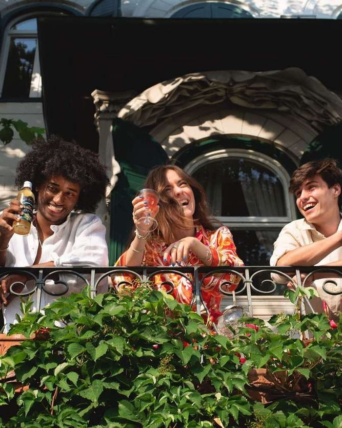 Tre ragazzi brindano con Intro Kombucha da un balcone fiorito