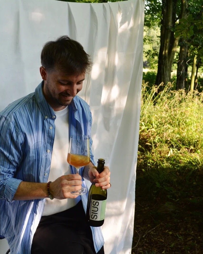 Michael Weissenegger di Sius Brewing apre una bottiglia davanti a un telo bianco, in un bosco